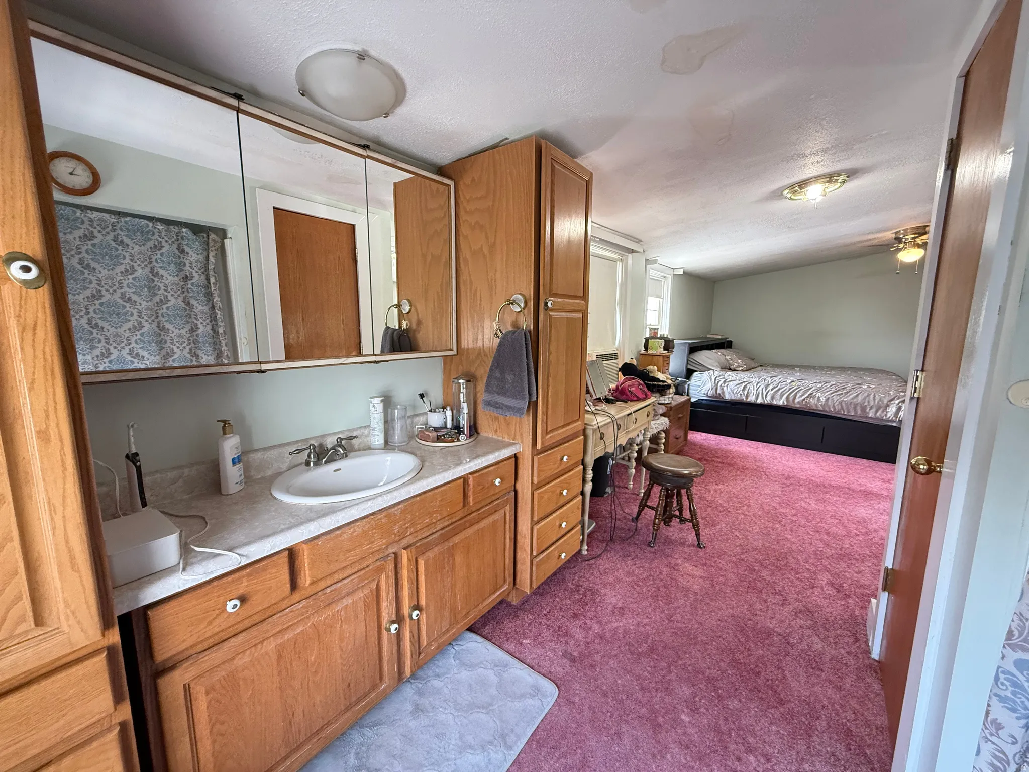 Primary Bathroom and Bedroom Suite featuring wood-finish cabinetry with ample storage, dual-sink vanity with ceramic basin and countertop, large mirrored medicine cabinet, carpeted flooring, and direct access to an additional bedroom space