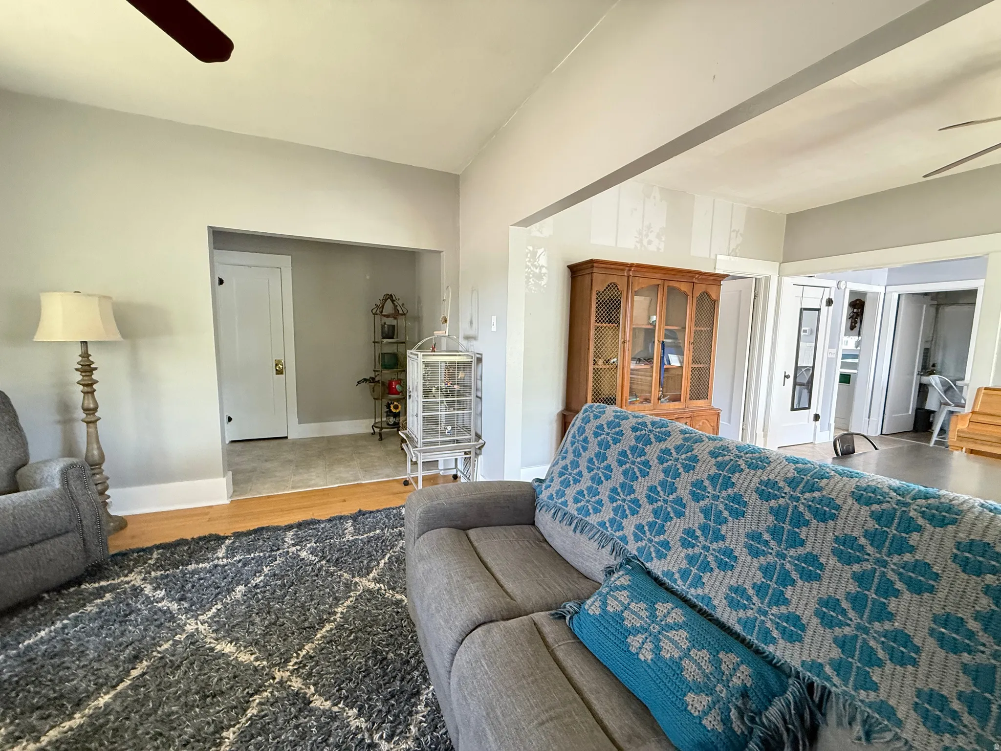 Spacious living area featuring neutral wall finishes, ceiling fan, wood-finish cabinetry with glass-front doors, and abundant natural light from multiple windows and openings throughout the room