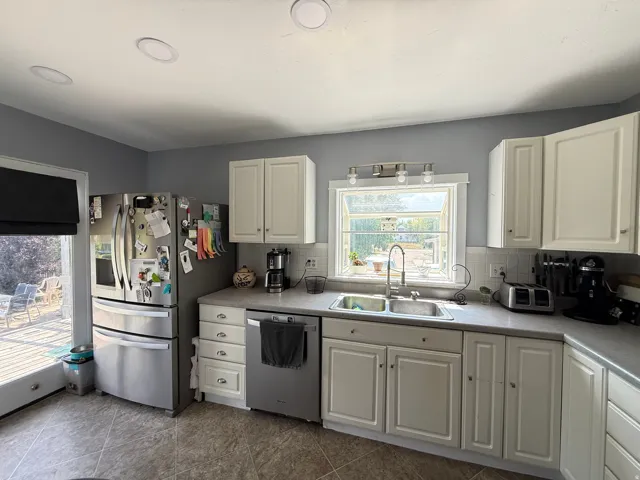 White cabinetry, a stainless steel refrigerator, and a stainless steel dishwasher complement the tiled flooring and recessed ceiling lighting