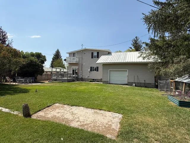 Expansive green lawn with a wood deck, balcony, detached garage with metal roof, and raised garden beds