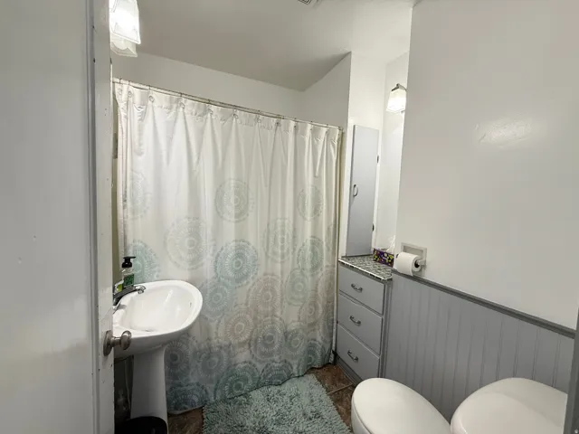Functional full bathroom featuring a pedestal sink, toilet, and bathtub with shower enclosure