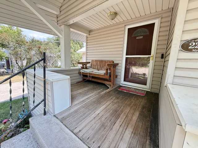Welcoming front porch featuring a wood-finish deck, metal railing with cable detailing, covered ceiling with recessed lighting, wooden bench seating, and direct entry through a dark-stained entry door
