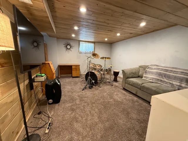 Versatile recreation room featuring wood-finish ceiling with recessed lighting, carpeted flooring, built-in cabinetry, and a flat-screen television mount