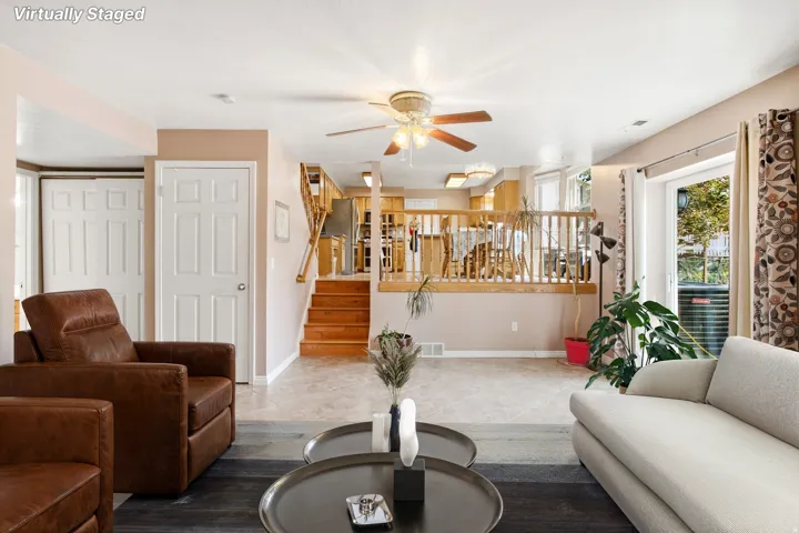 Light-toned walls with ceiling fan, wood-finish flooring, and natural wood staircase with railing