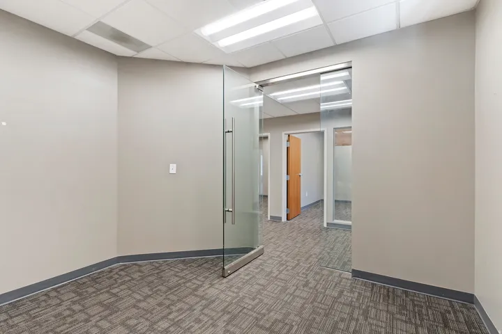 Glass entry door with stainless steel hardware, neutral wall finishes, patterned carpet, and acoustic tile ceiling with fluorescent lighting