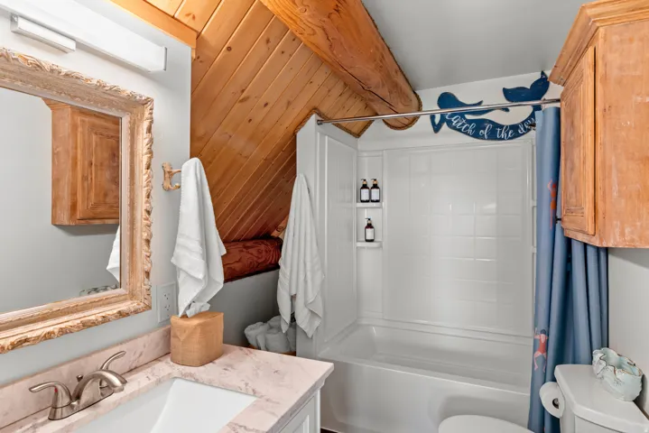Charming bathroom featuring vaulted wood-finish ceiling, marble-topped vanity with wood-framed mirror, and white subway tile shower surround with chrome fixtures