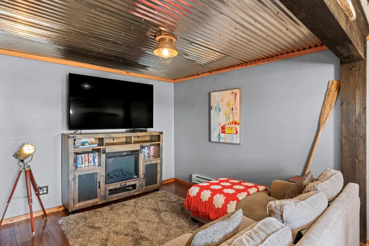 Corrugated metal ceiling, exposed wood beams, wood-finish flooring, and a built-in media console with an electric fireplace