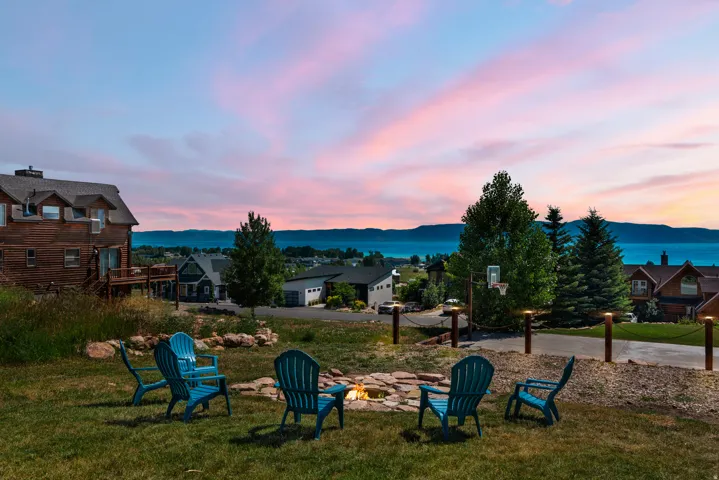 Expansive backyard featuring a stone-lined fire pit, manicured lawn, and mature trees