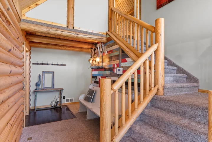 Log wall construction and exposed beam ceiling, raw wood staircase with carpeted treads, and a built-in bench with a rustic wood accent wall