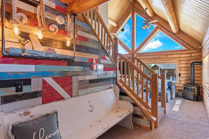 Log cabin interior with exposed wood beams, a prominent staircase with wood railing, and triangular-shaped windows