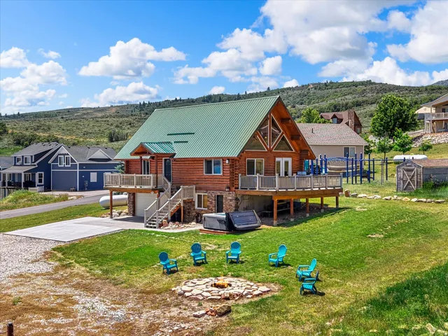 Charming timber-frame residence with a distinctive green metal roof and covered front porch, situated on expansive grounds featuring a manicured lawn, mature landscaping, and a designated fire pit area with Adirondack seating
