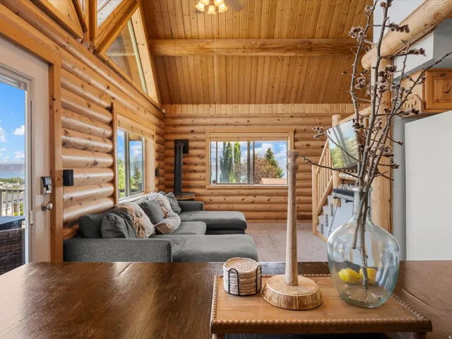 Open-concept log cabin interior showcasing exposed timber beam construction, vaulted wood-paneled ceiling, and expansive windows framing mountain and forest scenery