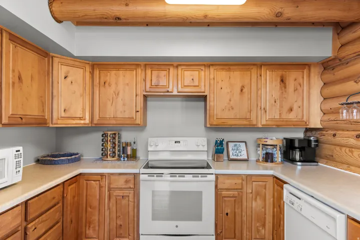 U-shaped kitchen with wood cabinetry, light-toned countertops, and white appliances including a built-in dishwasher