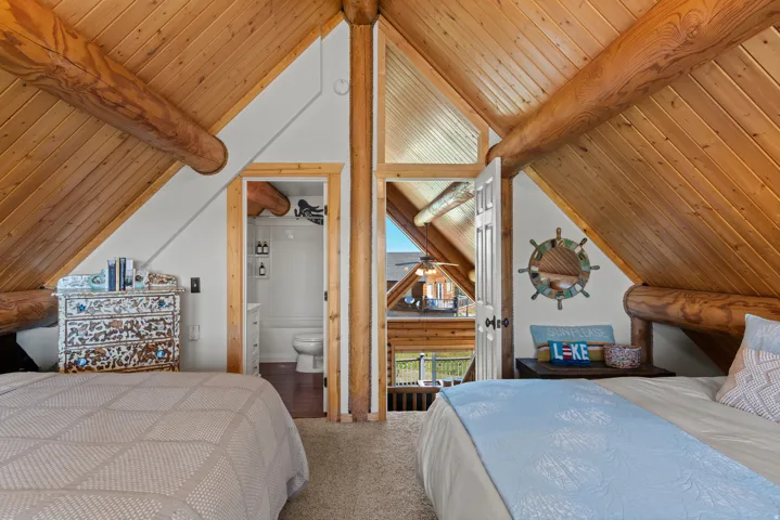 Vaulted wood-paneled ceilings with exposed log beams, carpeted flooring, and a private attached bathroom with a toilet and vanity