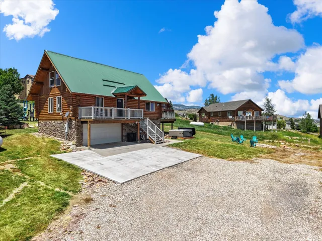 Rustic log cabin with green metal roof and stone chimney detail, featuring a covered front porch with white railings and an attached two-car garage