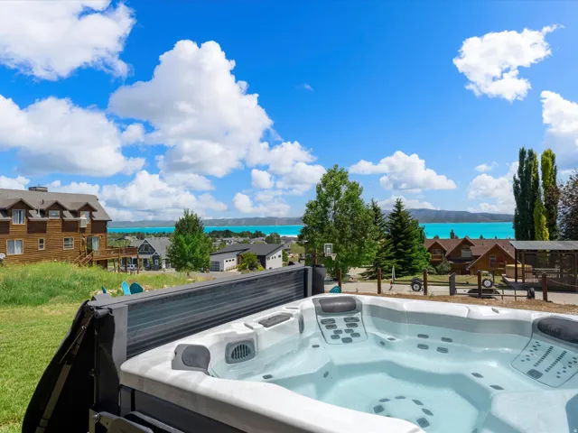 Spa-inspired hot tub with multiple jets and integrated controls overlooking manicured grounds, mature evergreen and deciduous trees, and turquoise water in the distance