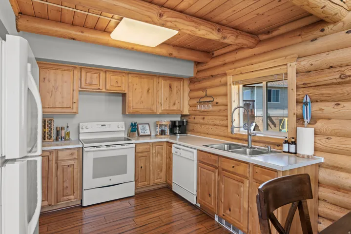 Rustic log cabin kitchen featuring custom wood cabinetry, stainless steel appliances including electric range and dishwasher, wood-finish flooring, and a spacious island with seating