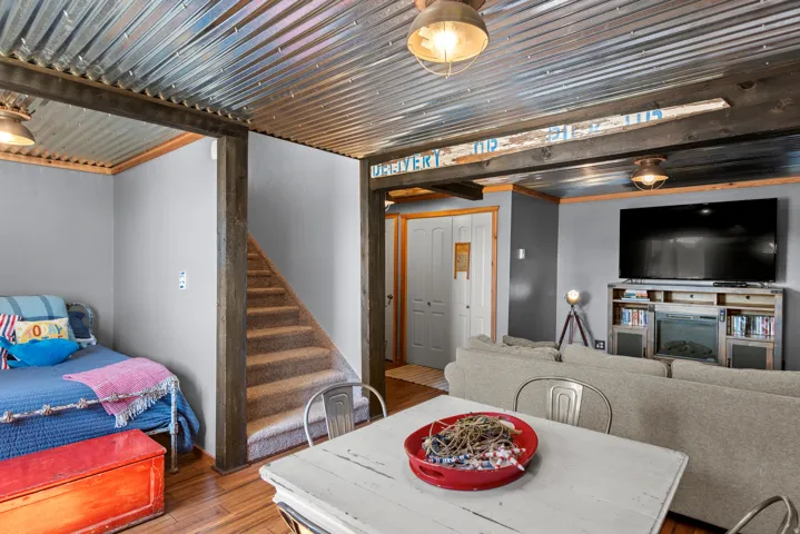 Corrugated metal ceiling with exposed wood beams, carpeted staircase, wood-finish flooring, and painted interior walls