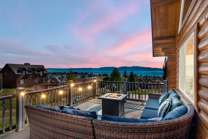 Expansive composite deck featuring curved woven rattan seating with cushioning, metal railings, and integrated outdoor heating—overlooking waterfront scenery and distant tree-lined shores
