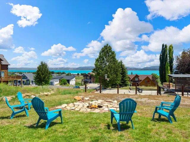 Expansive grounds featuring a level lawn with mature evergreen trees, a stone-ringed fire pit area, and multiple Adirondack seating arrangements