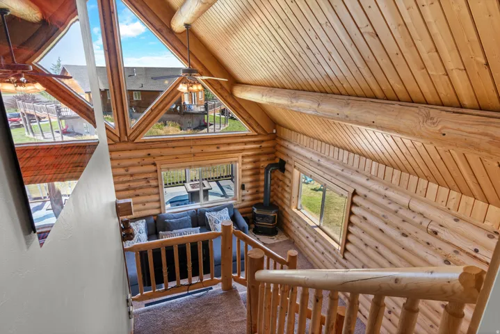 Vaulted wood-paneled ceiling with exposed wood beams, extensive natural wood log walls, and a freestanding wood-burning stove
