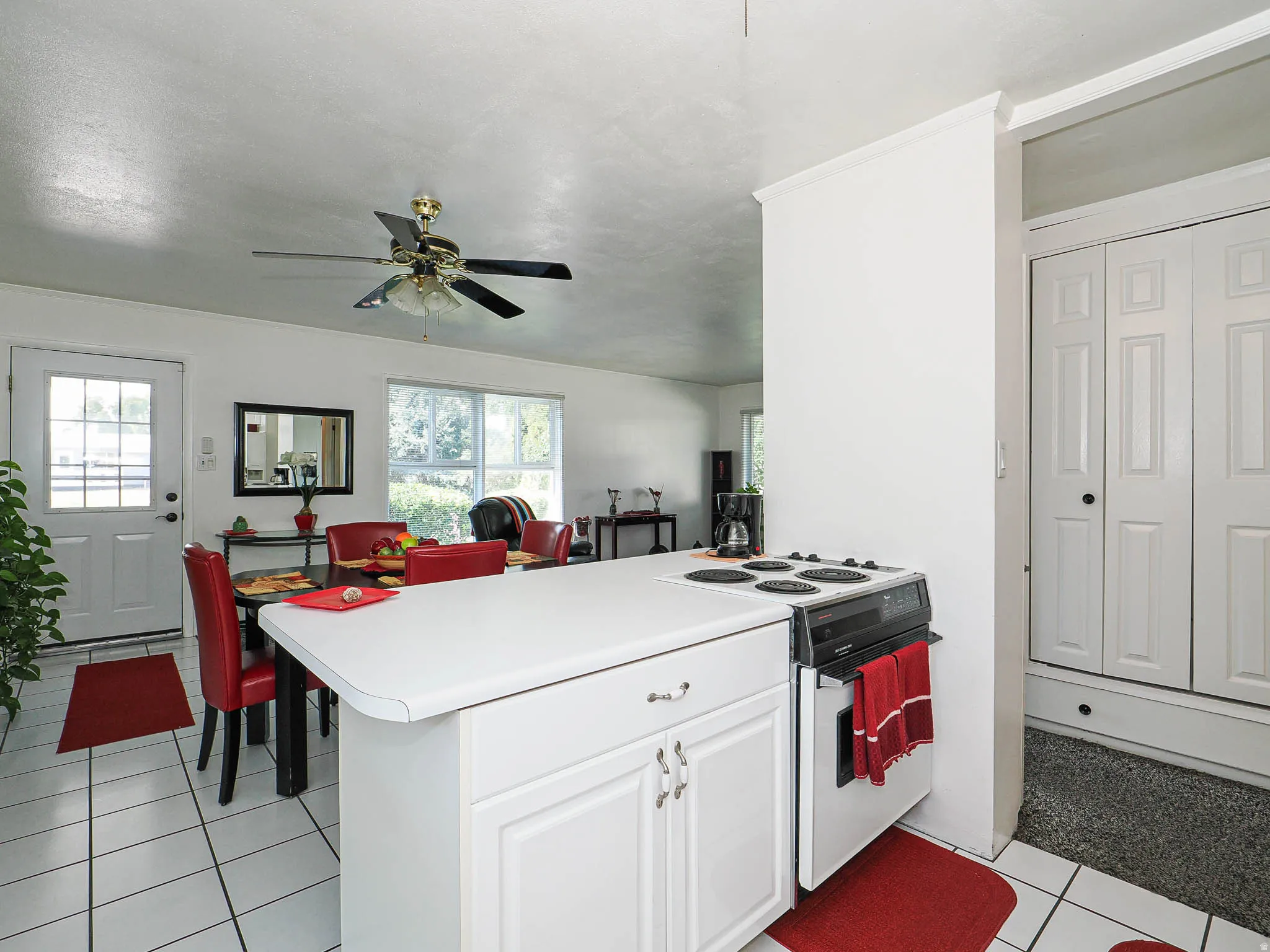 Open kitchen featuring a large white island with ample counter space, ceramic tile flooring, stainless steel appliances, ceiling fan with integrated lighting, and abundant natural light from multiple windows throughout the space