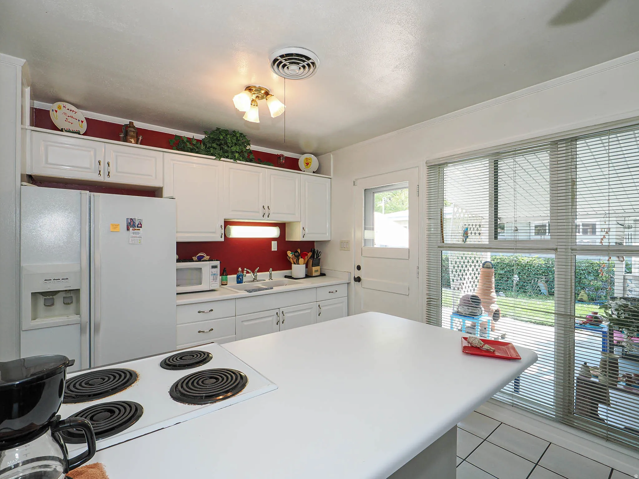 White cabinetry, solid surface countertops, white tile flooring, ceiling-mounted light fixture, and a large window overlooking the exterior
