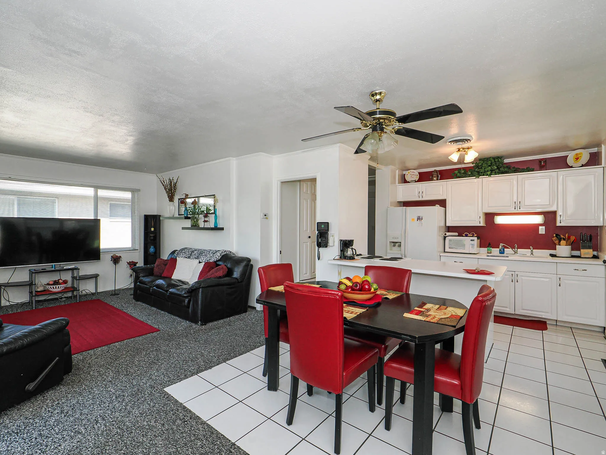 Open-concept living and dining area featuring tile flooring, a ceiling fan with integrated lighting, and a black dining table with red upholstered chairs
