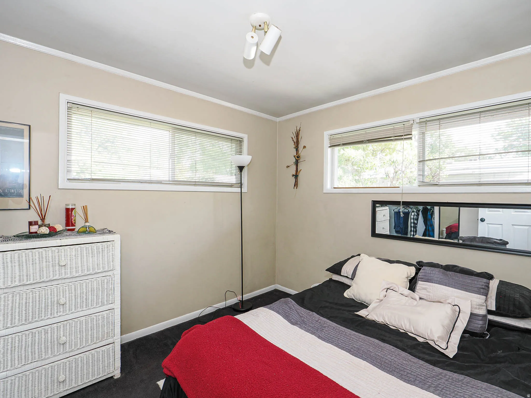 Comfortable secondary bedroom featuring dual windows with cellular shades, wood-finish flooring with dark tile accents, white cabinetry with wicker-textured fronts, and built-in shelving with open storage cubbies
