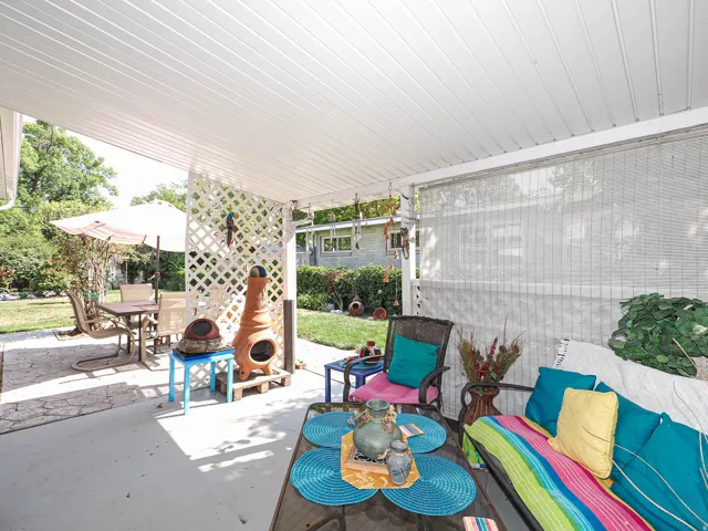 Covered patio with white beadboard ceiling and ceiling fan, featuring a blue tile-top bistro table, built-in bench seating with colorful cushions, and access to the fenced yard beyond