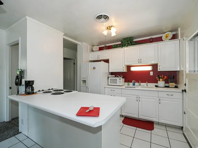 Bright kitchen featuring white cabinetry with hardware accents, a white quartz island with seating space, stainless steel appliances including a refrigerator with ice and water dispenser, a bold red tile backsplash, and ceramic tile flooring throughout
