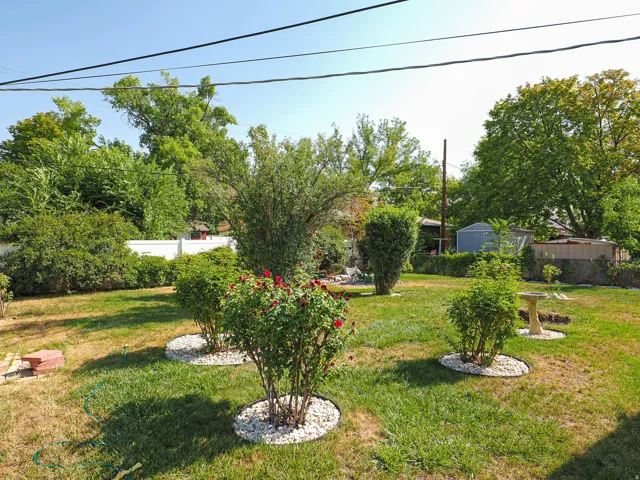 Spacious backyard featuring mature landscaping with established trees, freshly mulched planting beds, and lush lawn space