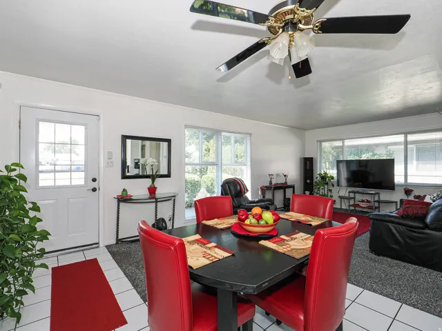 Open-concept living area featuring tile flooring, a ceiling fan with brass accents, and abundant natural light from multiple windows and glass doors