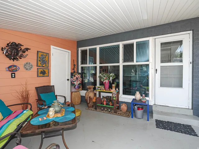 Covered porch with metal-framed glass doors and sidelights, corrugated metal ceiling, concrete flooring, and decorative wall-mounted artwork on the orange shiplap accent wall