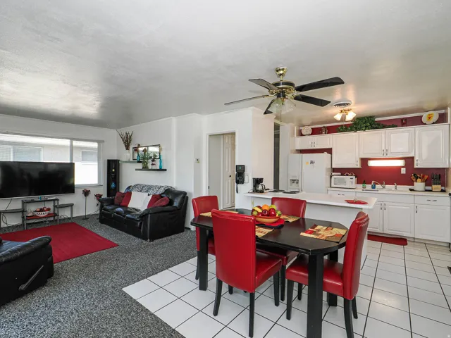 Open-concept living and dining area featuring tile flooring, a ceiling fan with integrated lighting, and a black dining table with red upholstered chairs