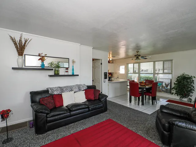 Open-concept living area featuring black leather seating, neutral carpeting with red accent rug, and ceiling fan