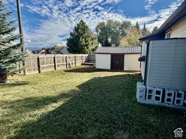 Backyard featuring a grass lawn, perimeter wood fencing, and a detached storage shed with a metal roof