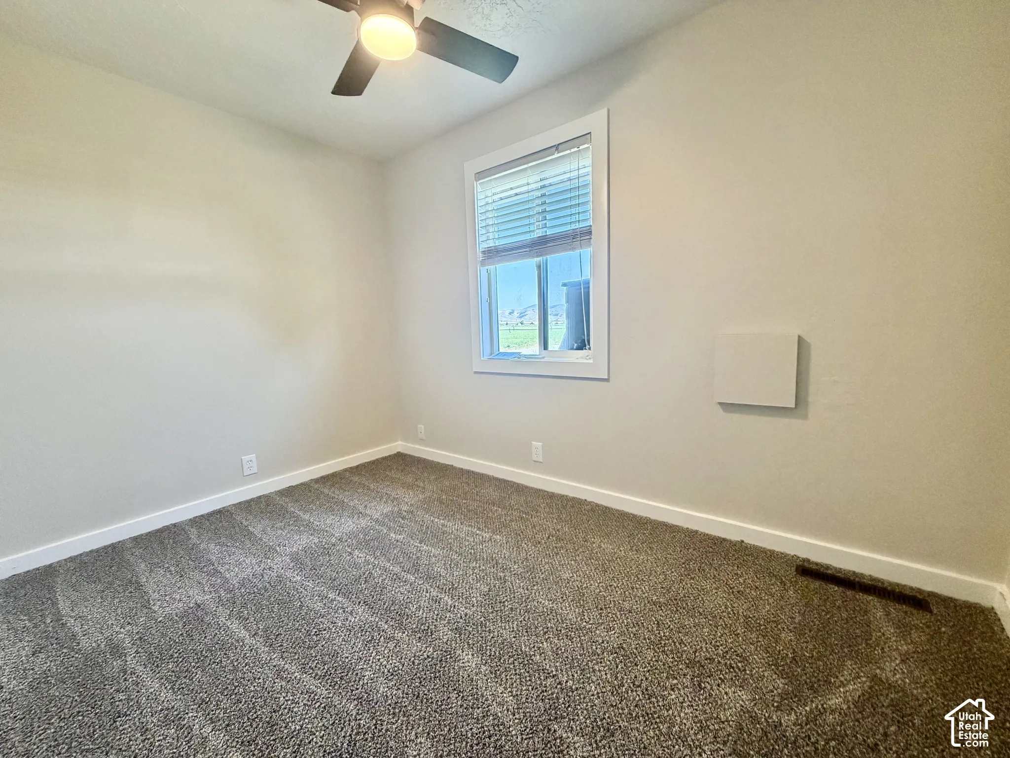 Bright bedroom featuring neutral wall finishes, carpet flooring, a ceiling fan with integrated lighting, and a large window with blinds providing natural light and privacy