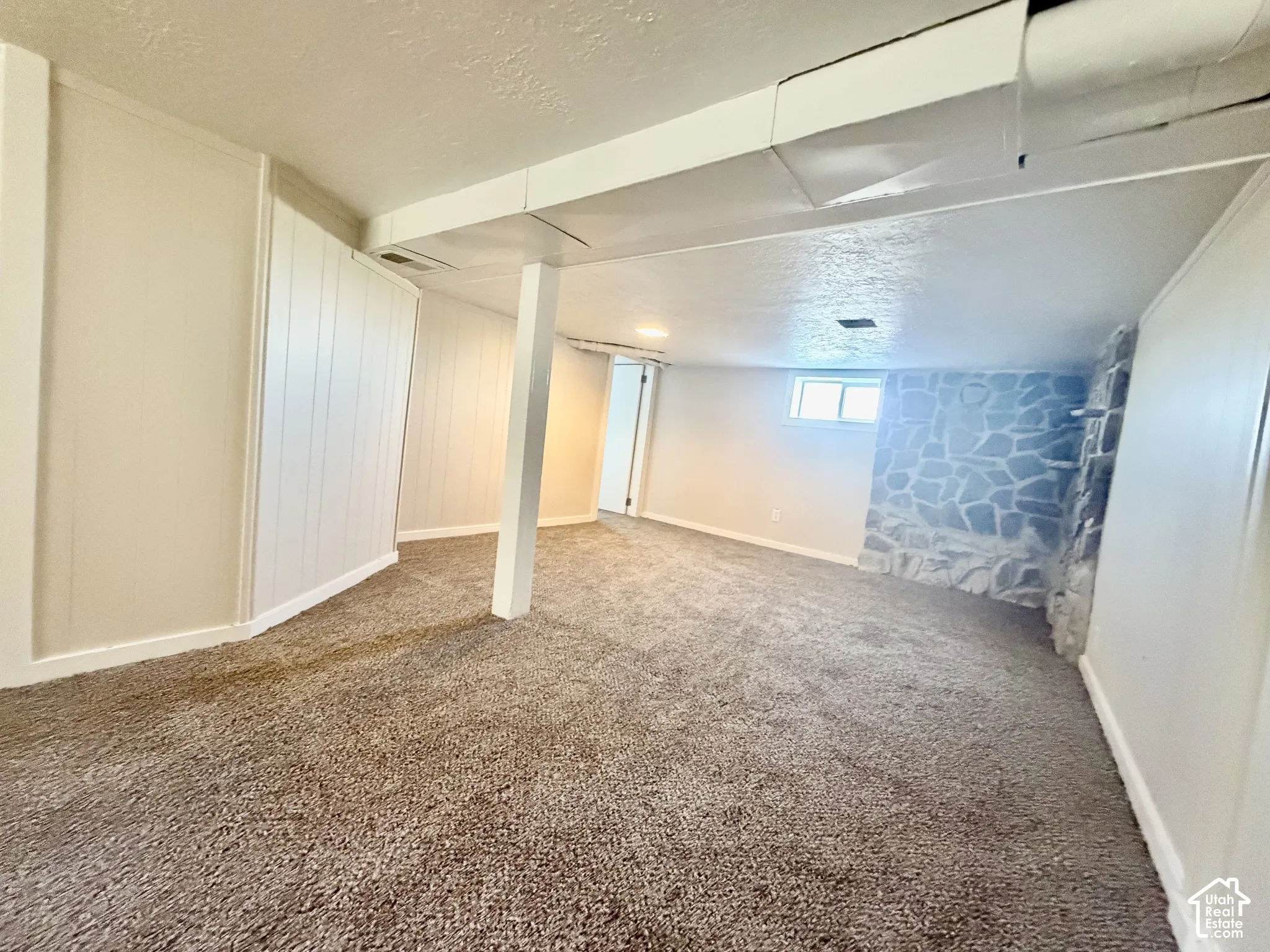 Spacious basement featuring neutral carpet flooring, white finished walls, exposed structural support columns, and recessed ceiling lighting throughout