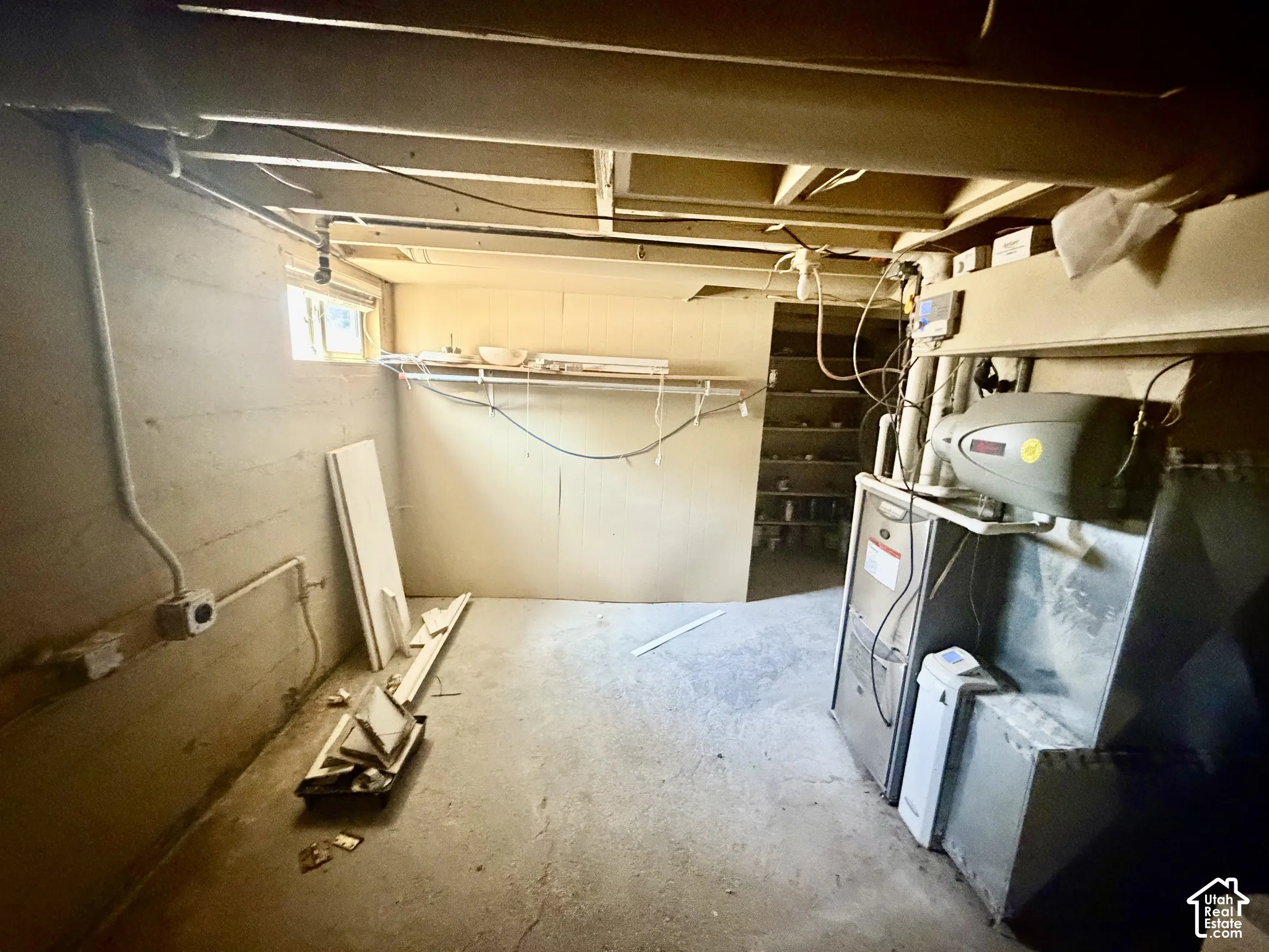 Unfinished basement with exposed ceiling joists, concrete foundation walls, and a utility window