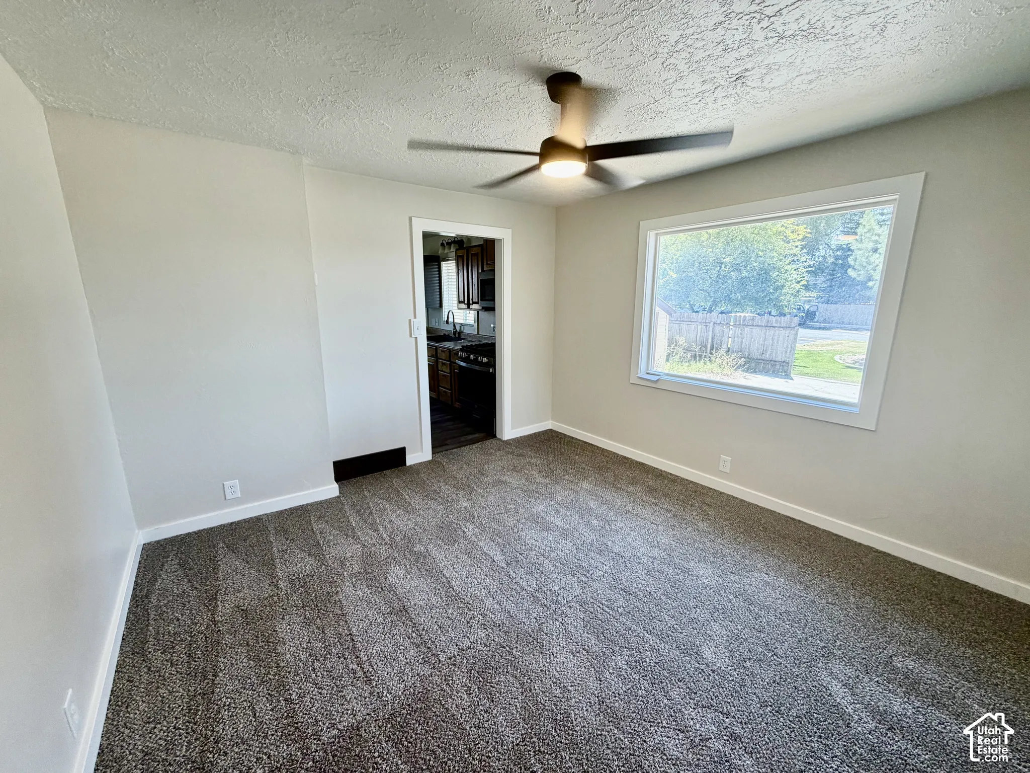Spacious room featuring fresh neutral walls, new carpet flooring, ceiling fan with integrated lighting, and large window with natural light exposure