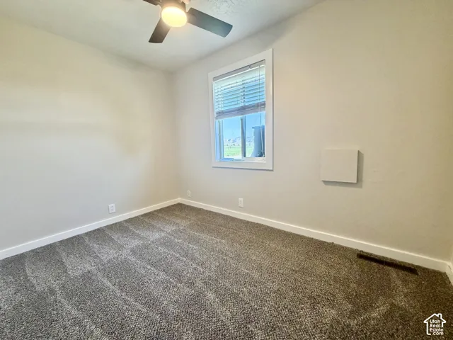 Bright bedroom featuring neutral wall finishes, carpet flooring, a ceiling fan with integrated lighting, and a large window with blinds providing natural light and privacy
