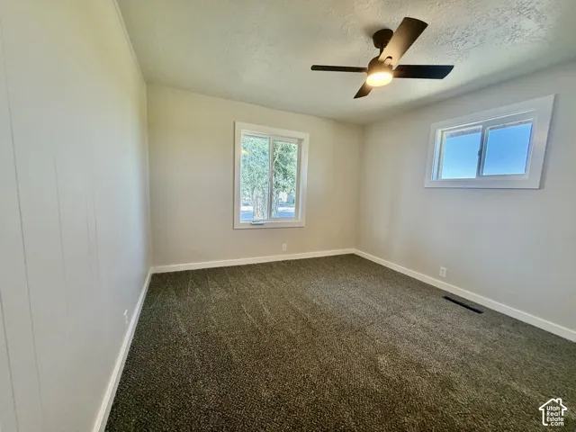Textured carpeting, two windows with white trim, and a ceiling fan with integrated lighting