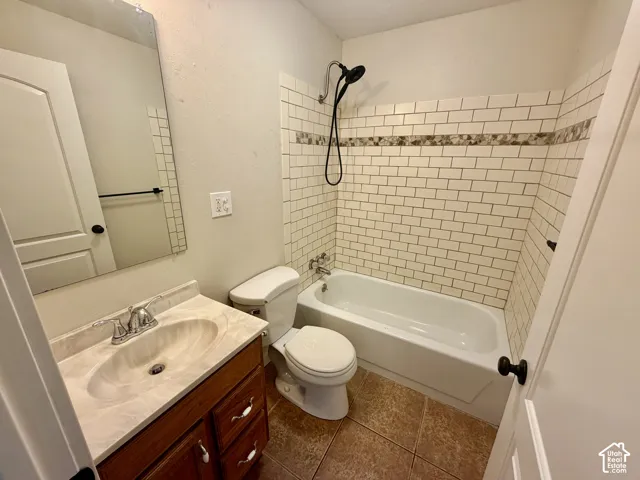 Updated full bathroom featuring ceramic subway tile walls with decorative border accent, white porcelain fixtures, wood-finish vanity with dual-sink basin, and alcove bathtub with shower combination