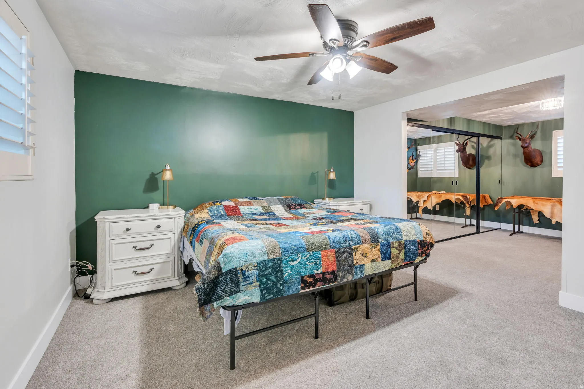 Primary bedroom suite featuring a green accent wall, ceiling fan with integrated lighting, carpeted flooring, mirrored closet doors, and an en-suite dressing area with natural light from multiple windows