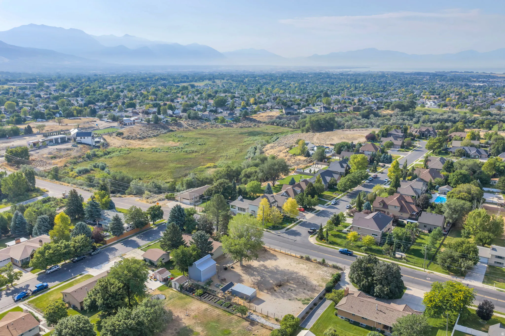 Aerial perspective showcasing a sprawling residential lot with mature landscaping, established trees throughout the neighborhood, and mountain vistas in the distance