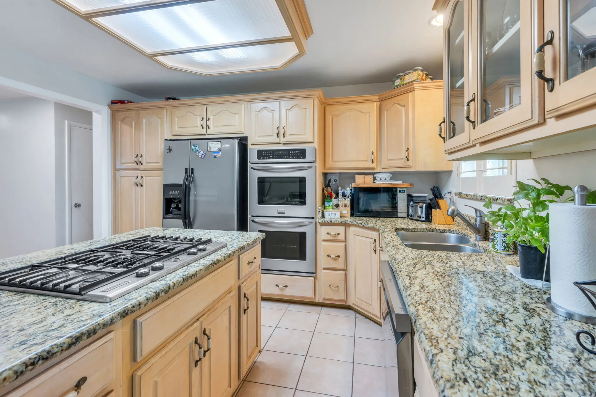 Chef's kitchen featuring natural wood cabinetry, granite countertops, a gas cooktop with stainless steel range hood, built-in wall oven, and stainless steel refrigerator with ice and water dispensers