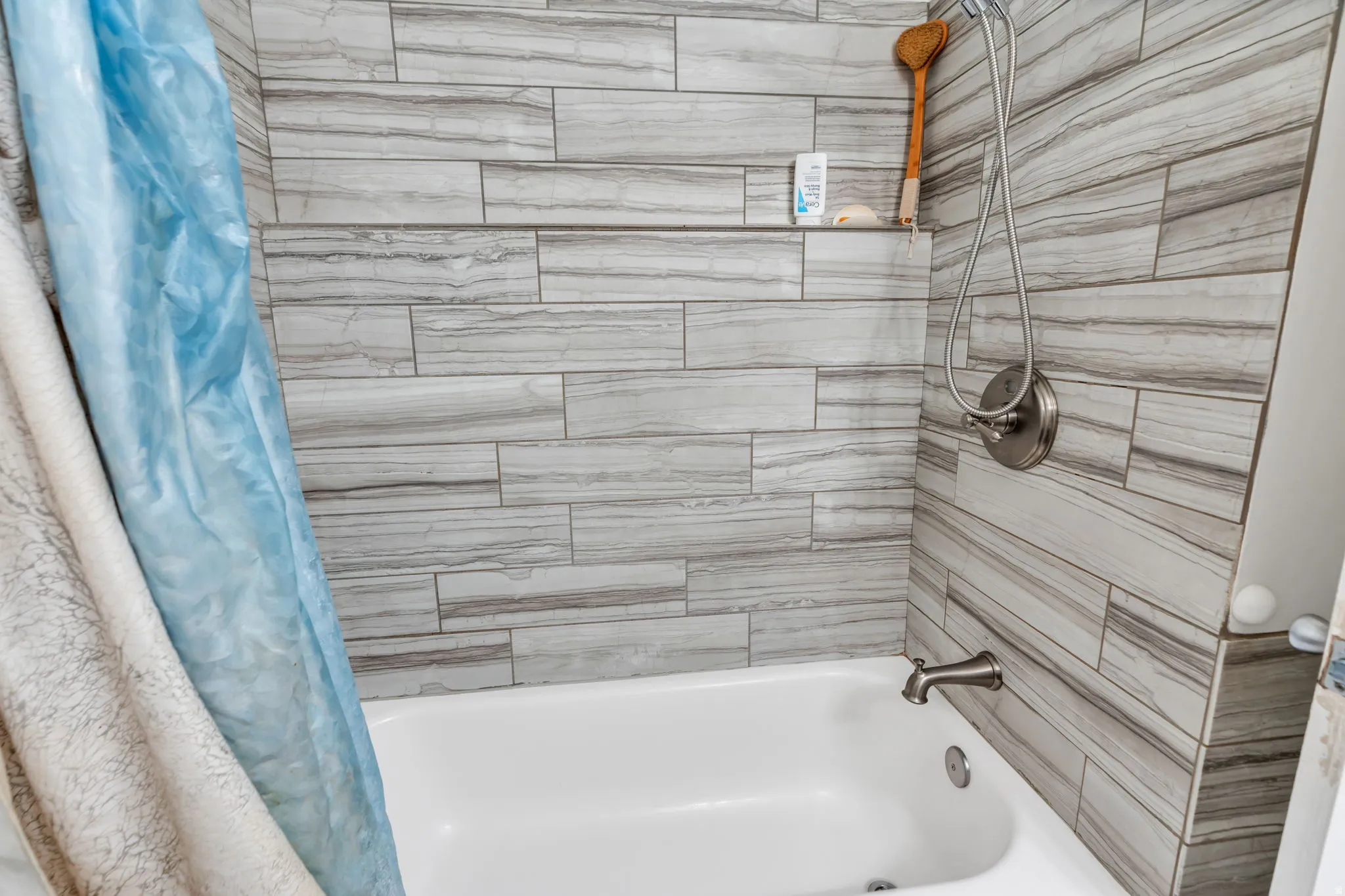 Updated bathroom featuring linear wood-finish tile surround, white soaking tub with chrome fixtures, and handheld showerhead