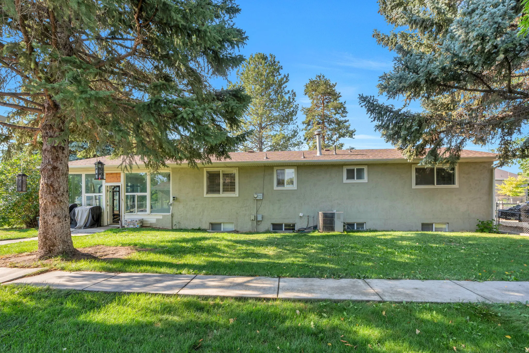 Charming single-story residence featuring a stucco exterior, multiple window openings for natural light, and a deep front lawn anchored by mature evergreen trees