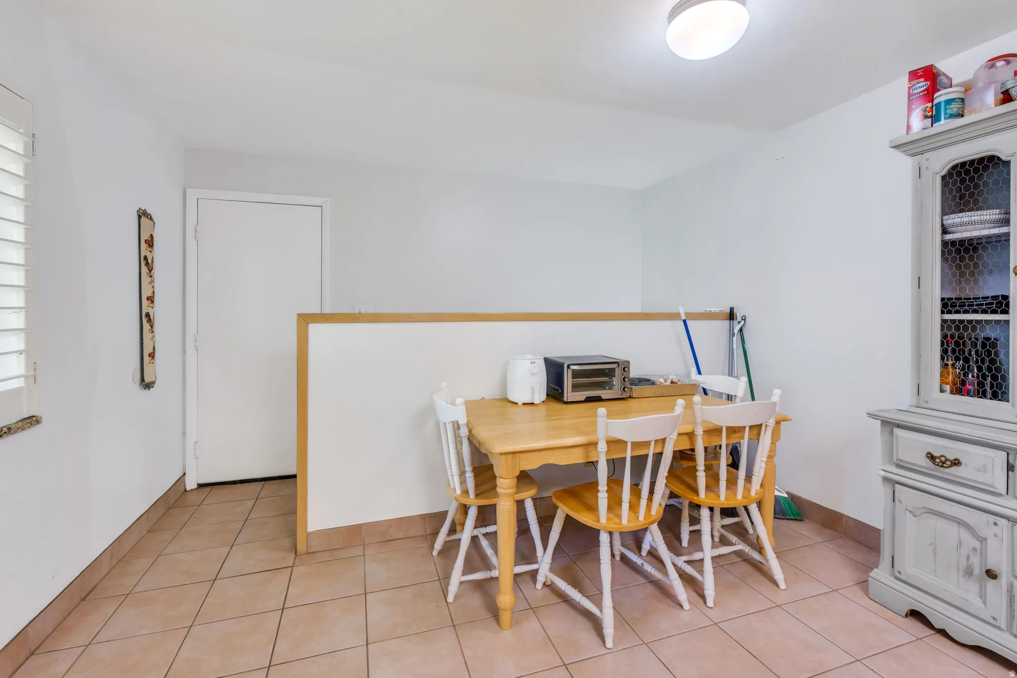 Casual dining area featuring a wood-finish table with seating for four, ceramic tile flooring, and abundant natural light from louvered windows